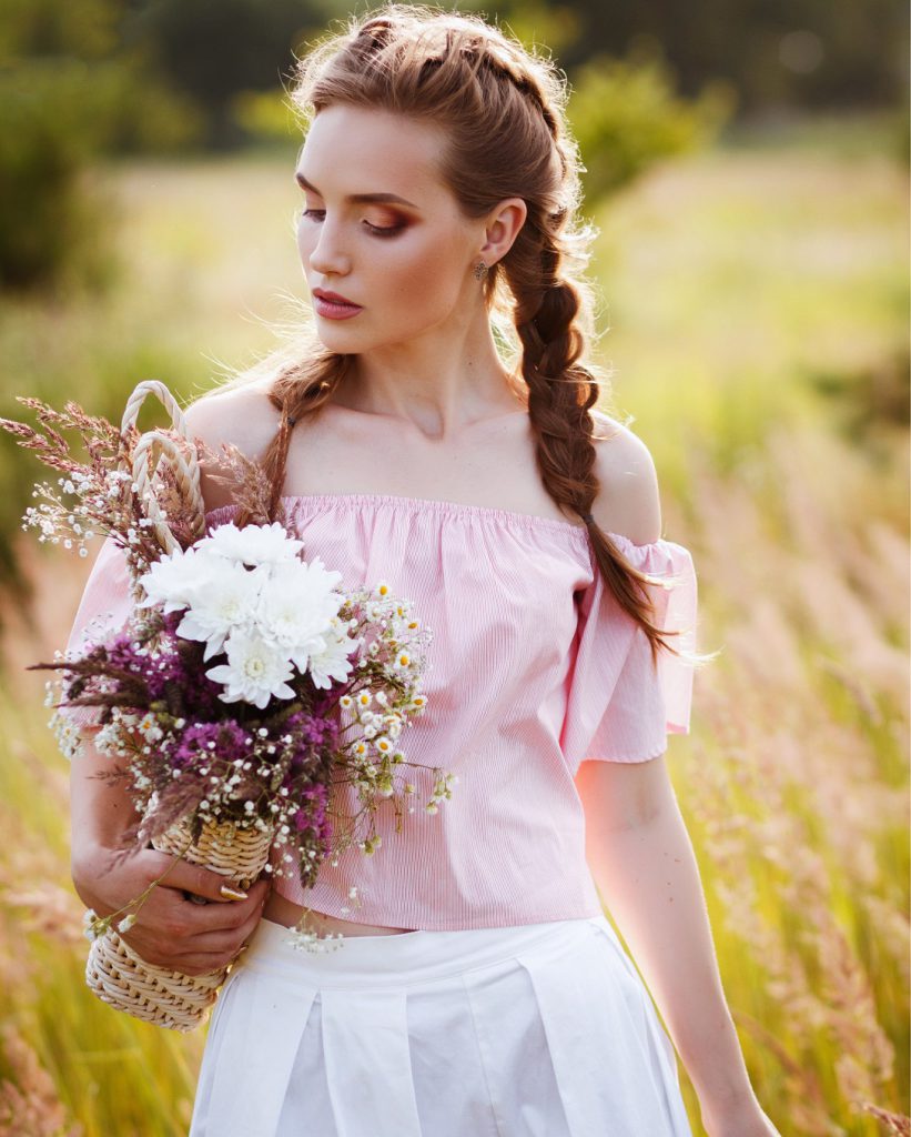 A woman with braided hair holding a bouquet of flowers while standing in a field