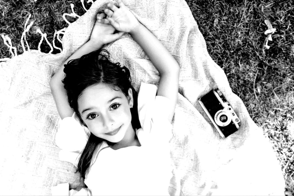 A young girl lies on the grass with black and white look and feel