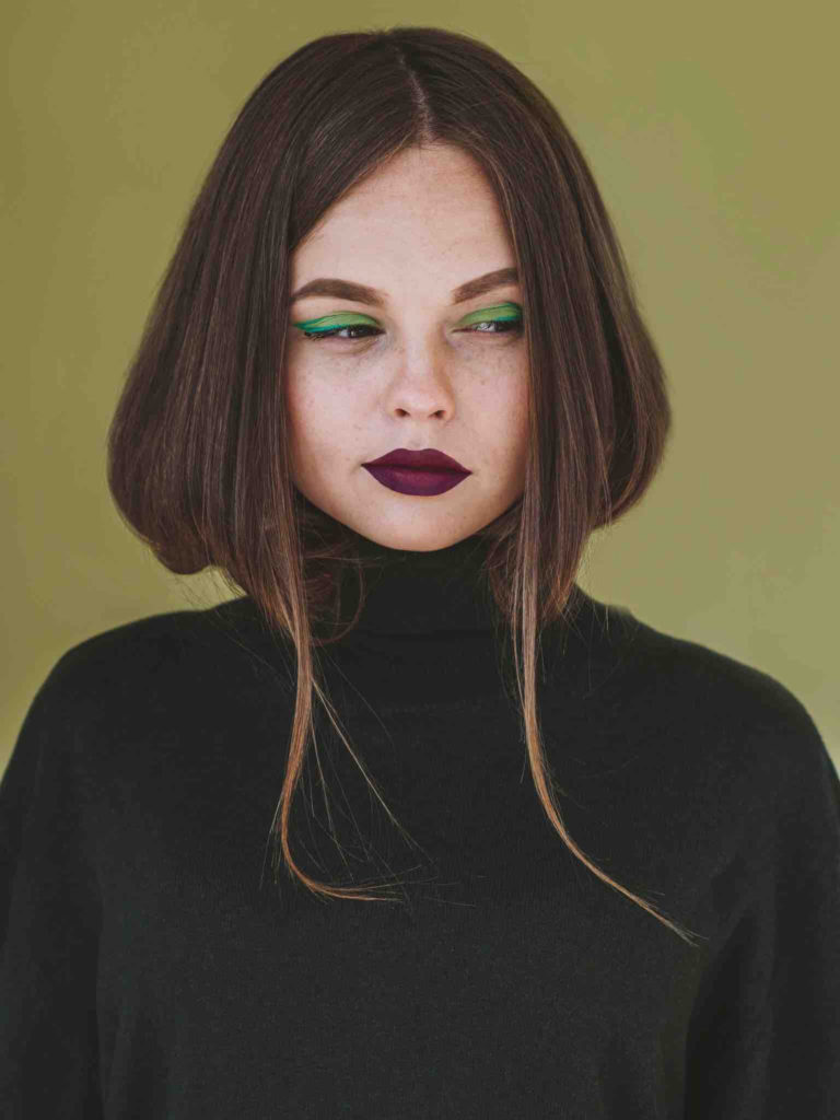 Woman in a studio with green eye shadow and dark brown hair looking from the side of her eyes